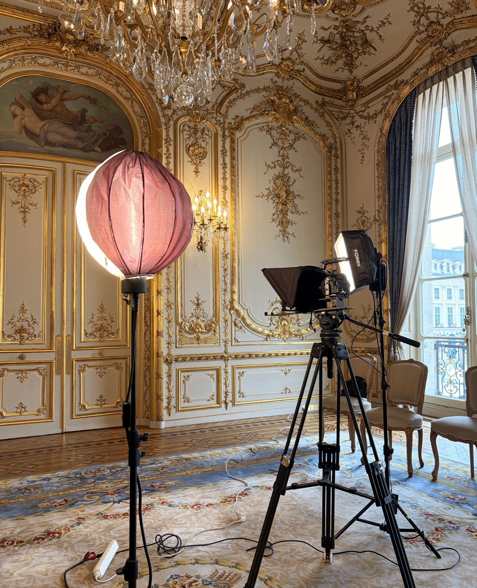 tournage-video-prestige-photographe-professionnel Matériel de tournage vidéo professionnel avec caméra sur trépied, prompteur et éclairage de studio installé dans un salon luxueux aux dorures de style classique.