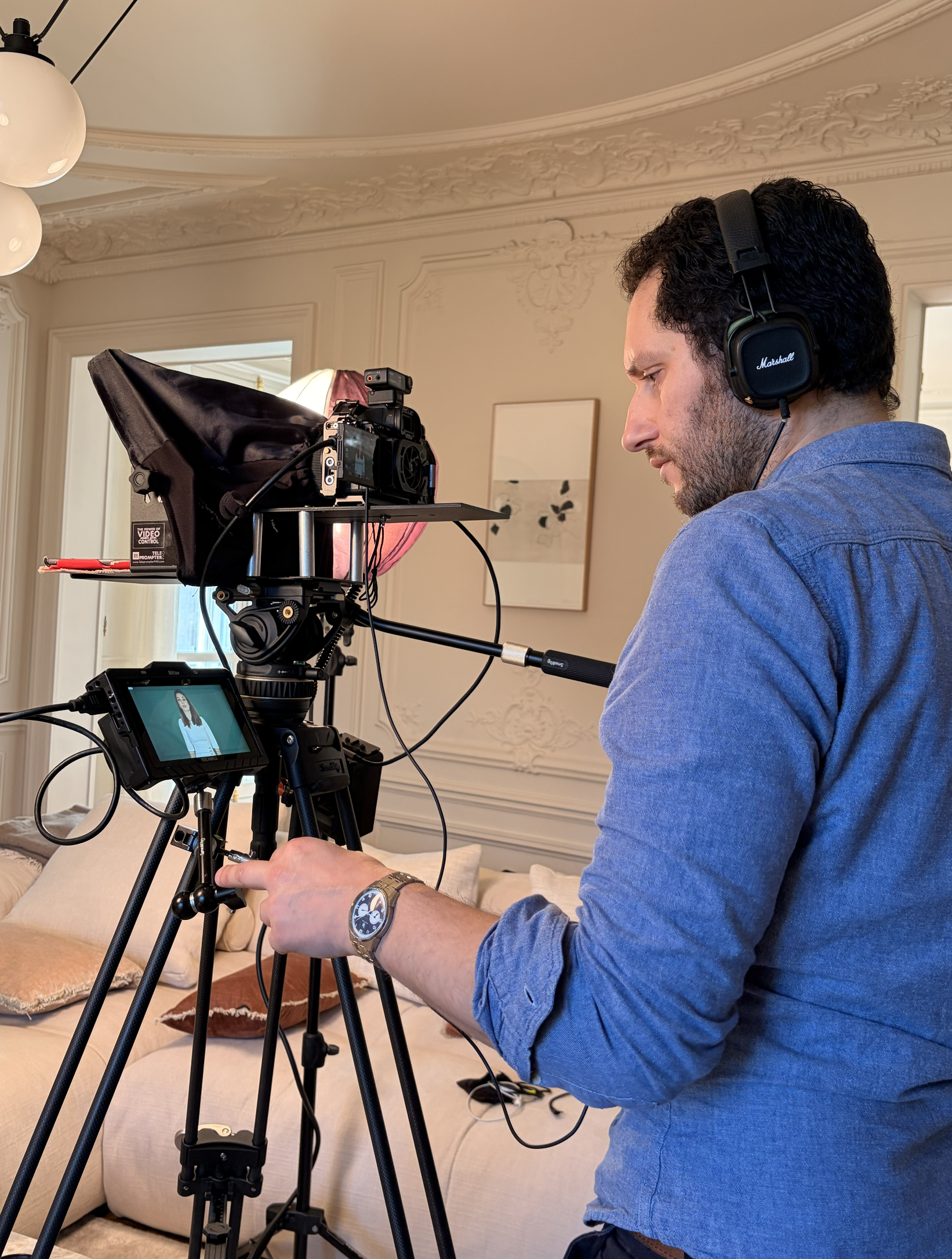 videaste-photographe-professionnel-tournage-corporate Un photographe professionnel et cadreur de profil portant un casque audio et réglant sa caméra de cinéma avec prompteur installée sur un trépied lors d'une interview.